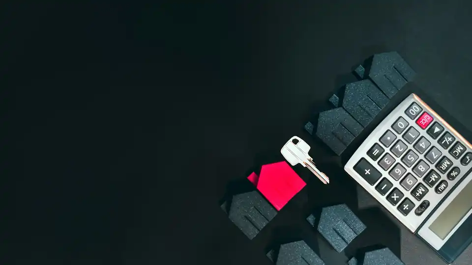 Key, small house model and calculator on a dark surface