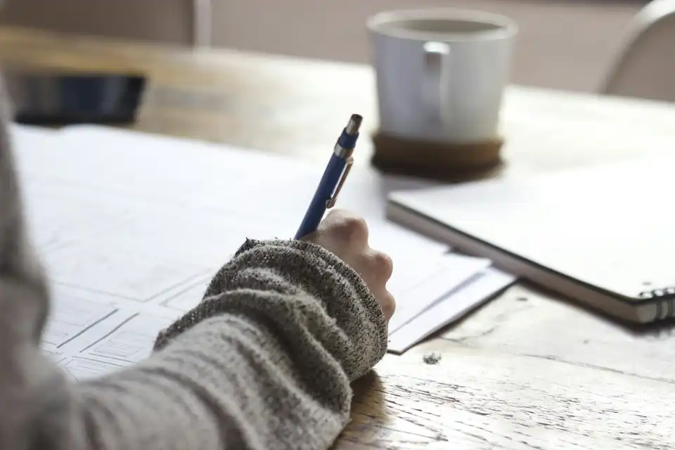Hand writing notes beside a coffee cup