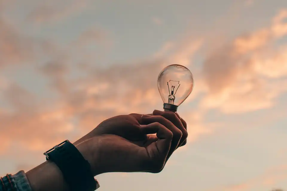 Hand holding a light bulb against the evening sky